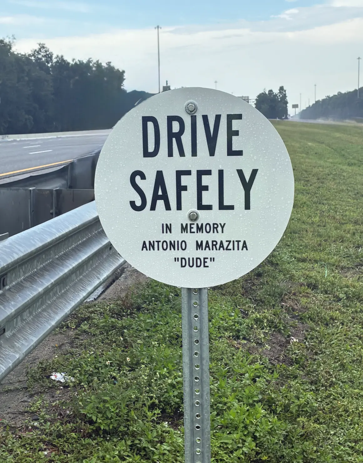 Circular roadside memorial sign reading Drive Safely In Memory Antonio Marazita Dude